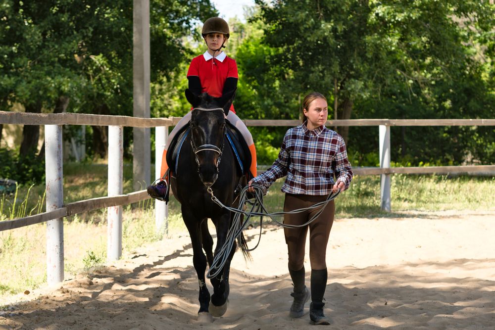 Young rider follows instructor's lead during equestrian lesson.