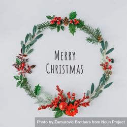 “Merry Christmas” surrounded with wreath made of branches of mistletoe and pine on light background 0KgE70