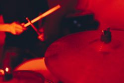Anonymous man with drumsticks playing on drums in redness
