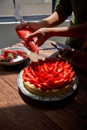 Crop chef decorating pie cake on table