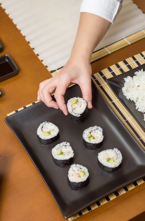 Top view of chef placing freshly made sushi rolls on plate