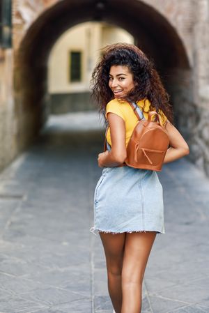 Smiling Arab woman walking through quiet street with arch, vertical