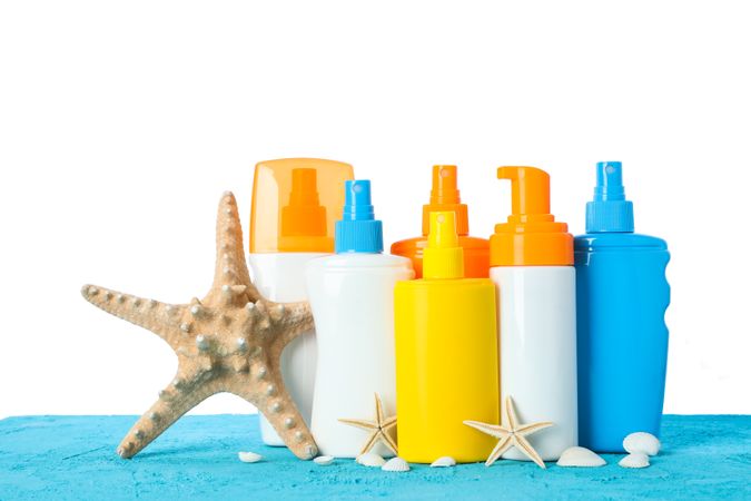 Different sunscreen sprays with starfishes and seashells on color table isolated on neutral background. Safe tan