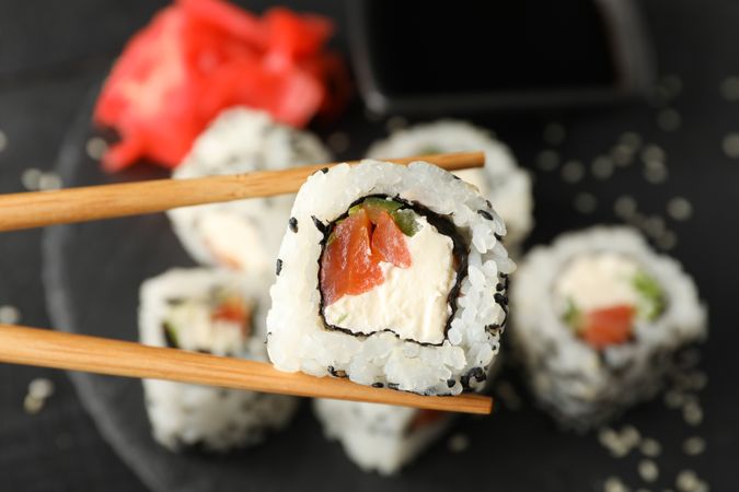 Chopsticks with delicious sushi roll, close up. Japanese food