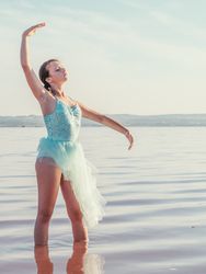 Ballerina in swimsuit with tutu performing classical position in water