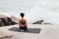 Female sitting next to the ocean sitting on knees gazing at the ocean