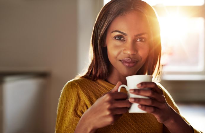 Portrait of Black woman with coffee in sunny room