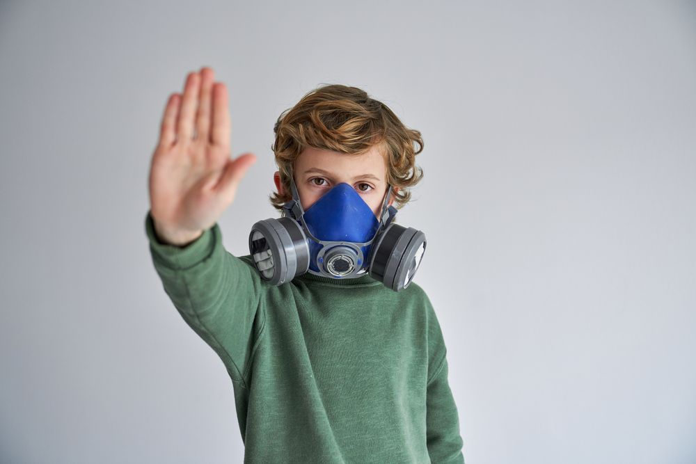 Calm child in respirator showing keep distance gesture in gray s