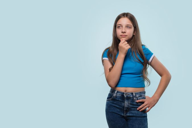 Thoughtful girl in blue top, contemplating, with hand on chin