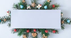 Pine tree branches with holiday decorations and blank center on blue pastel