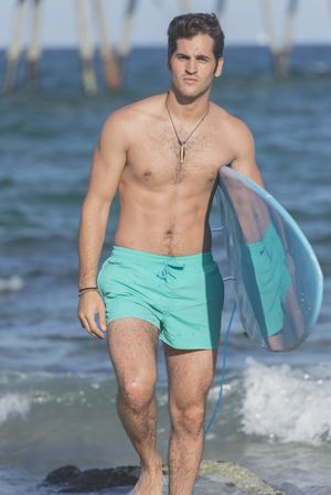 Front of male surfer with blue board in front of the sea