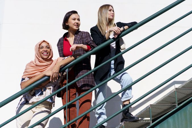 Multi-ethnic women friends, in stylish outfit and hijab on outdoor staircase