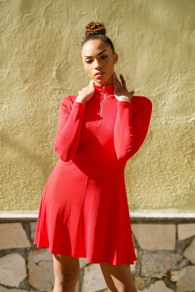 Serious female in casual red dress standing outside