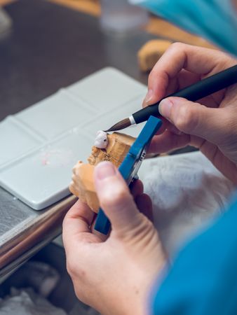 Crop female dental technician covering implants with ceramic