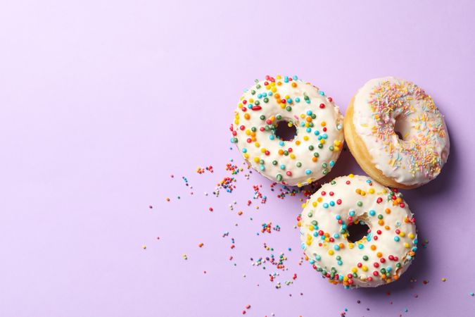 Three tasty donuts on violet background, top view