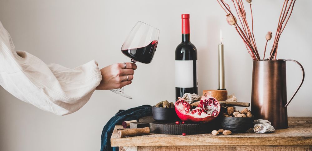 Rustic setting of women swirling wine, with cheese, long candles, pomegranate, and dried poppies