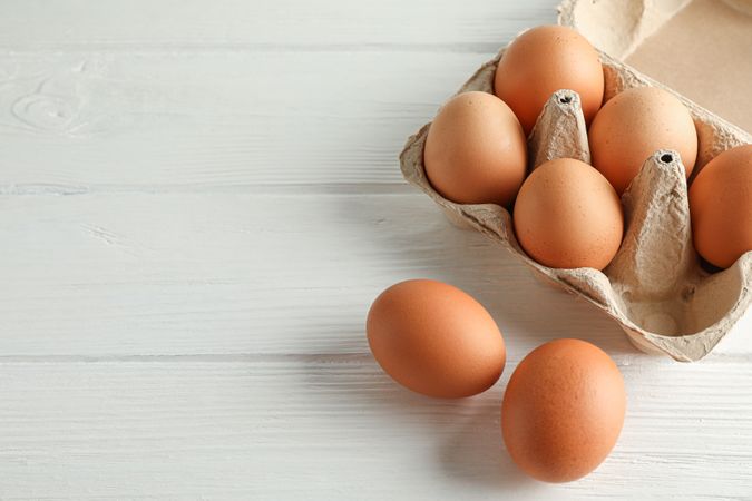 Brown chicken eggs in carton box on light background, space for text