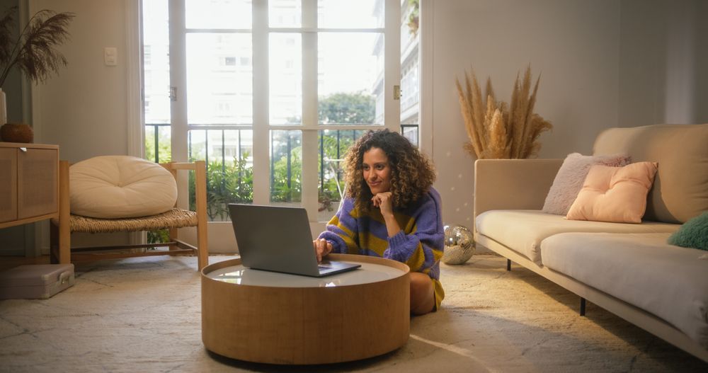 Portrait of Smiling Young Woman Working from Home on Laptop Computer in Sunny Cozy Apartment.
