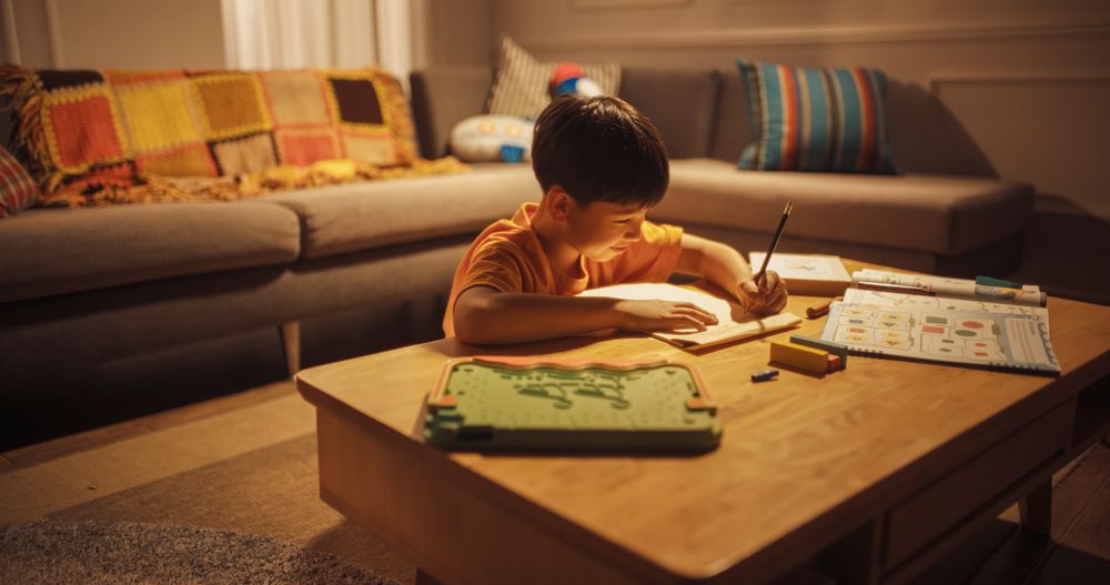 Portrait of a Cute Little Korean Boy Thinking and Writing in his Notebook in a Living Room During Evening.