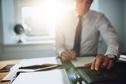 Man sitting at desk and writing with a calculator in sunny office