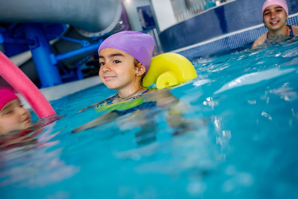 Cheerful girl in hat smiling and swimming in pool in water park