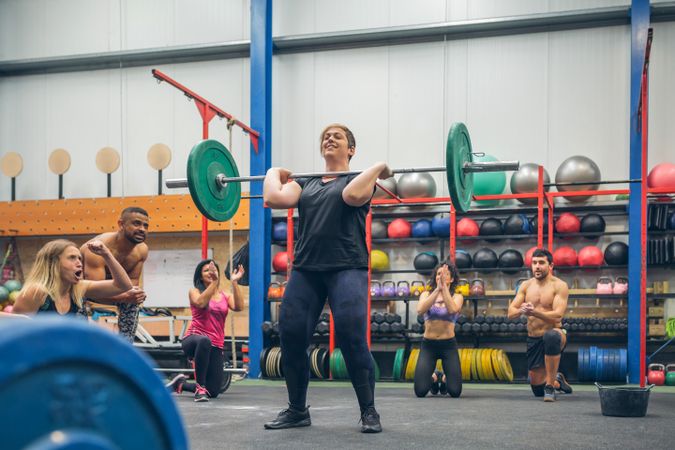 Proud woman weightlifting while her gym mates cheering her on