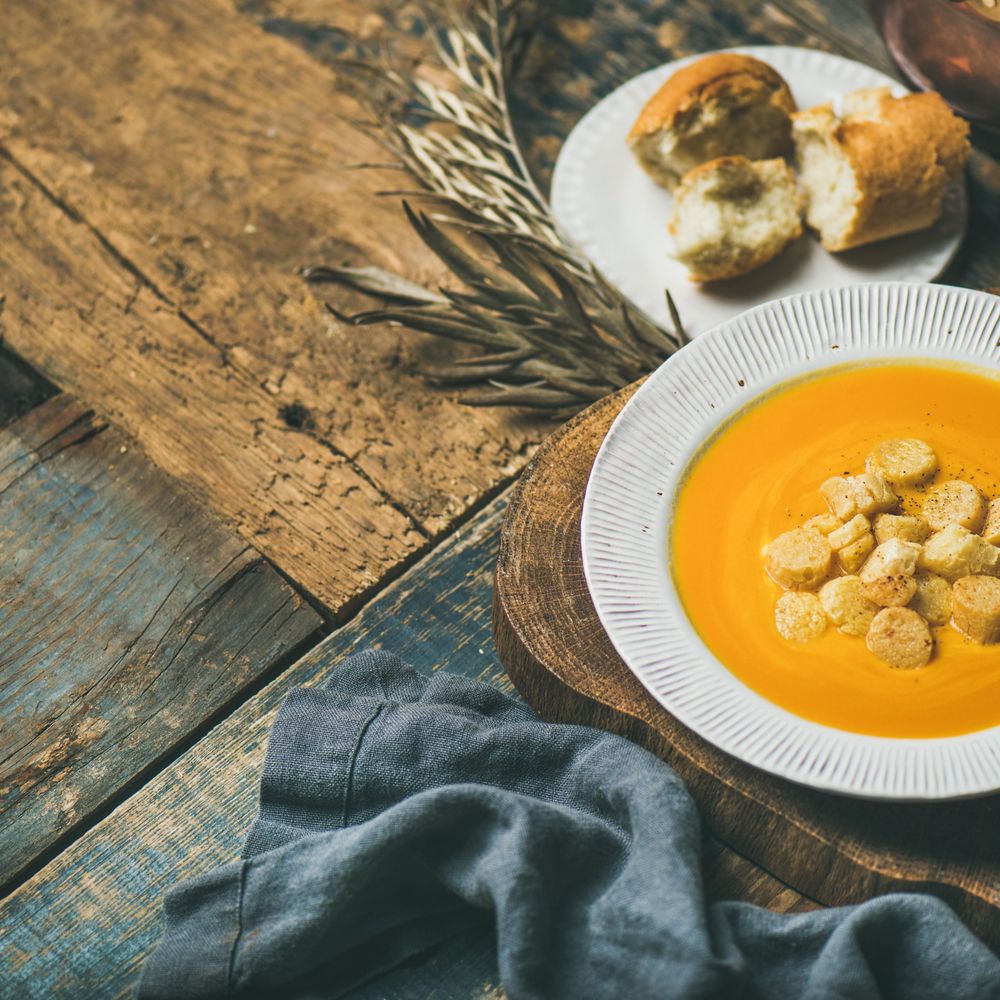 Pumpkin soup with croutons, and bread on wooden table, square crop