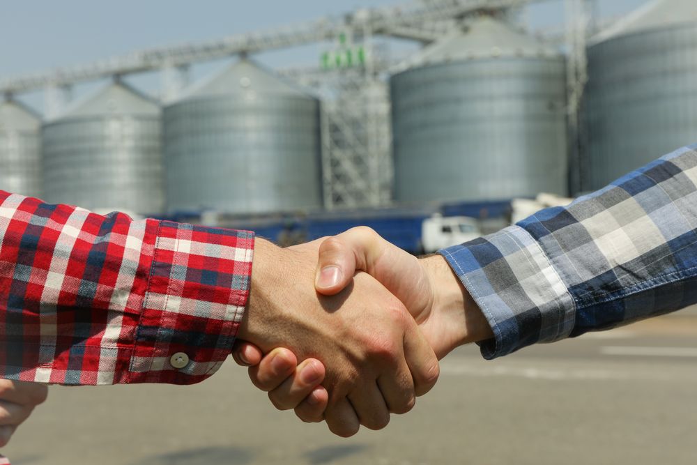 Businessmen shake hands against silos. Agriculture business