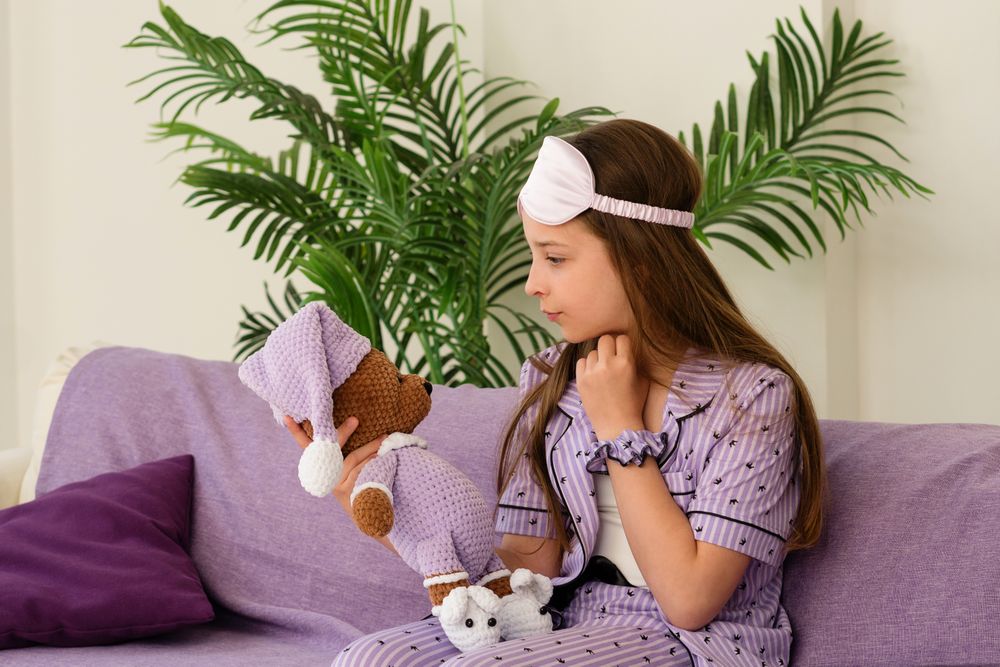 Girl seated on couch, holding teddy bear with care.