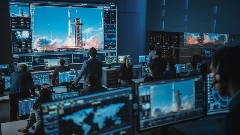 Aerospace Command Center Buzzes With Activity as Team Monitors Rocket Launch on Giant Screen.