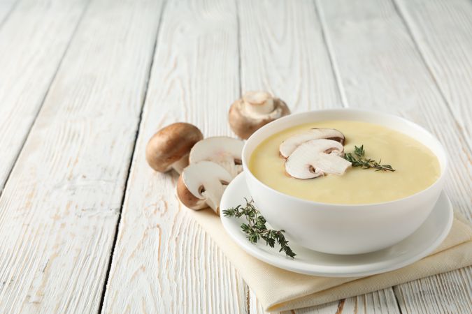 Bowl of creamy mushroom soup with herbs on napkin on wooden table, copy space