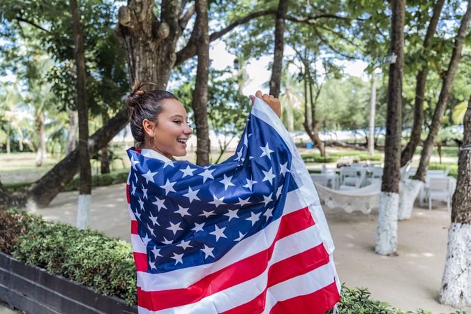 Content woman smiling wrapped in American flag walking along park