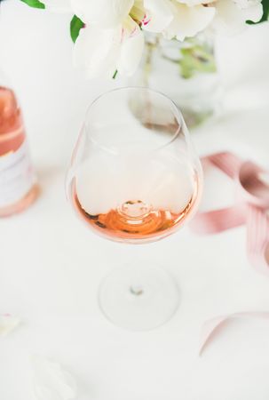 Glass of pink rose wine in center, and bottle, flowers and ribbon in background