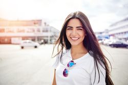 Portrait of woman with long flowing brown hair outside on a street with parked cars