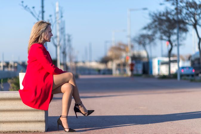 Side view of blonde woman sitting on a bench and looking in the distance