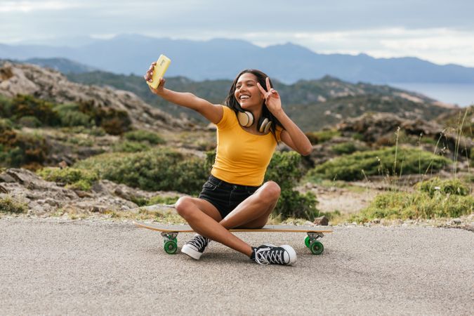 Delightful woman on longboard taking selfie on smartphone