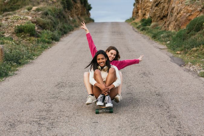 Happy diverse women riding longboard on road