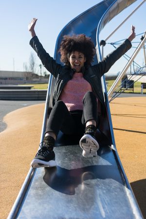 Woman with afro hair jumping down a slide.