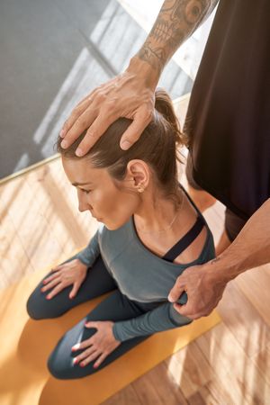 Unrecognizable coach helping woman during yoga lesson