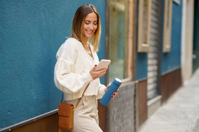 Smiling woman with reusable bottle using smartphone on street