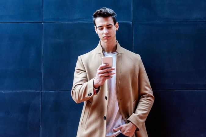 Young man in the center wearing winter coat looking at phone screen against dark wall