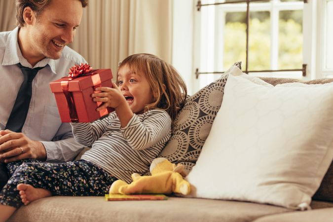 Father and daughter sitting on a sofa looking at a gift box
