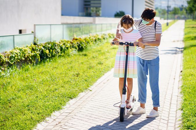 Mother teaching daughter how to ride a scooter outdoor