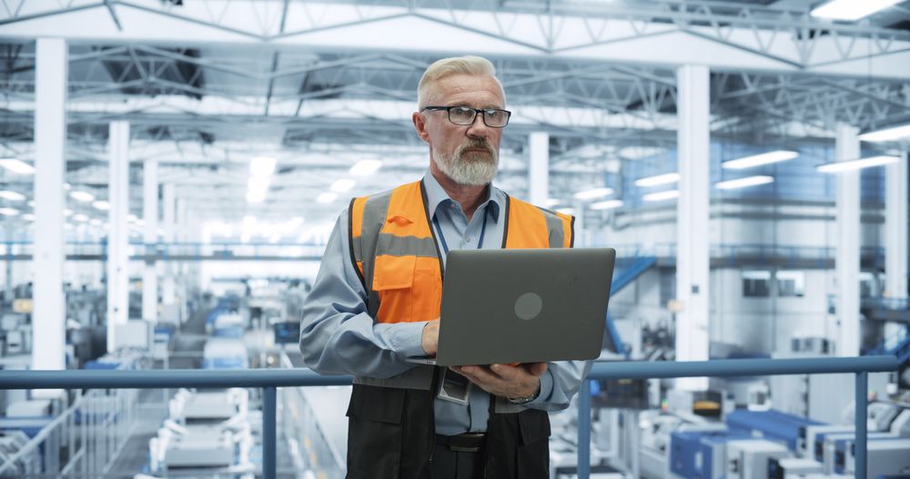 Portrait of a Thoughtful Engineer Monitoring and Analyzing Conditions at a Modern Electronics Factory with Automated Robots Working with the Help of Artificial Intelligence Software
