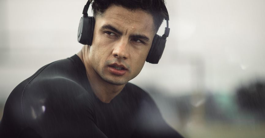 Young man in activewear with headphones on looking away