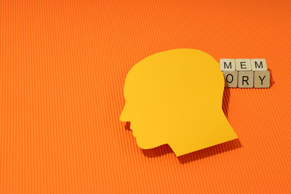 Orange duotone flat lay of head with shadow with the word “memory” in wooden blocks, copy space