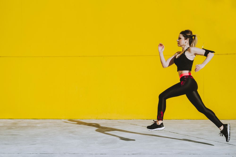 Woman with earphones running near wall