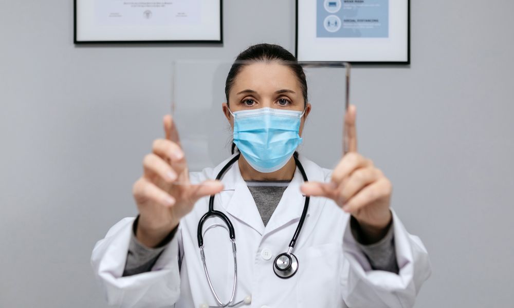 Female doctor with protective mask holding transparent tablet