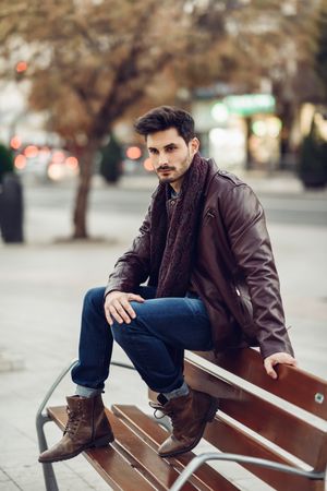 Man in leather coat sitting on top of bench