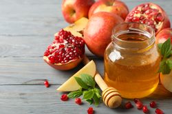 Honey pot surrounded by slices apples and pomegranate on grey table with text for space